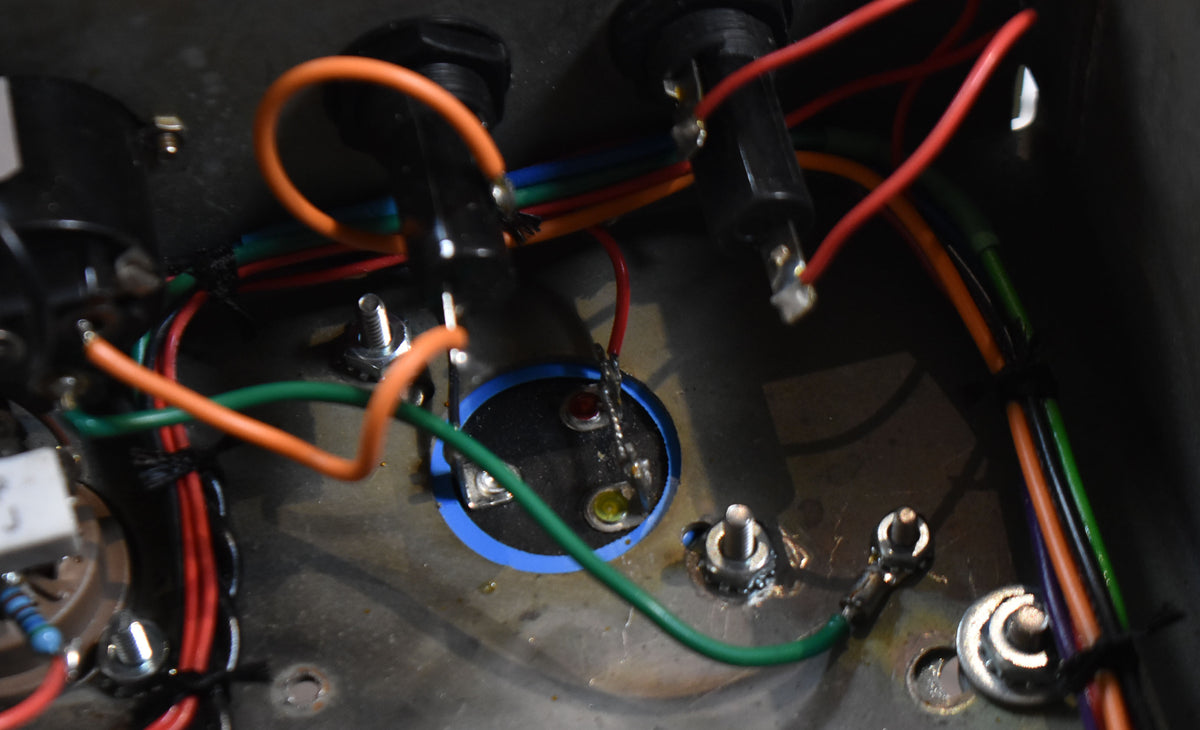 Close-up of the amp's internal wiring, showing colorful wires, solder joints, and two small red and yellow indicator lights.