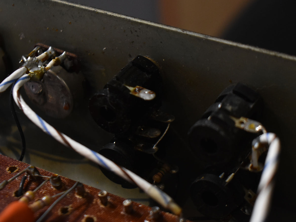 Close-up of the amp's internal wiring, showing two black input jacks, a potentiometer, and a brown circuit board with soldered components.