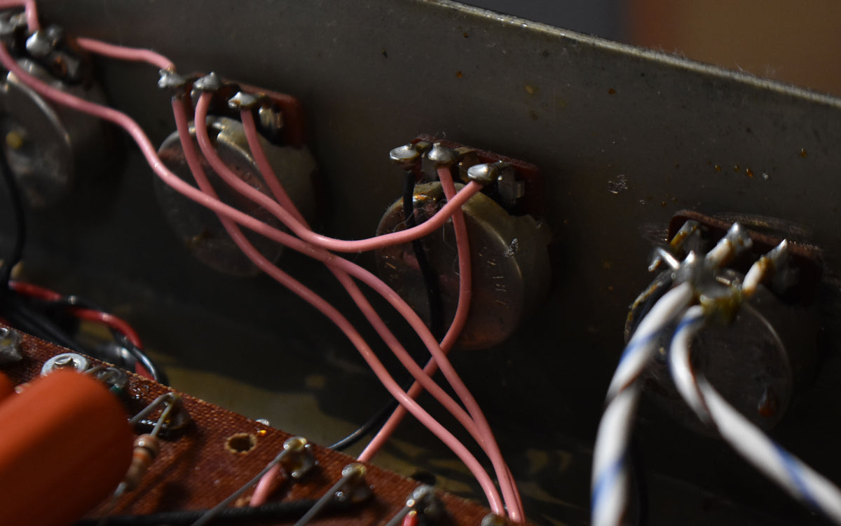 Close-up of the amplifier's internal wiring, showing several silver potentiometers connected by pink and white wires to a brown circuit board.