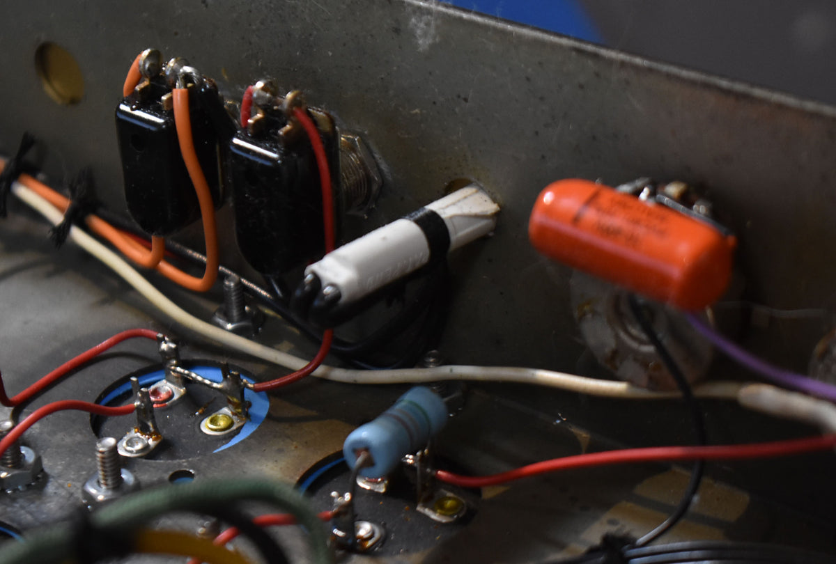 Close-up of the amp's internal wiring, showing two black switches, a white and an orange capacitor, and various colored wires.