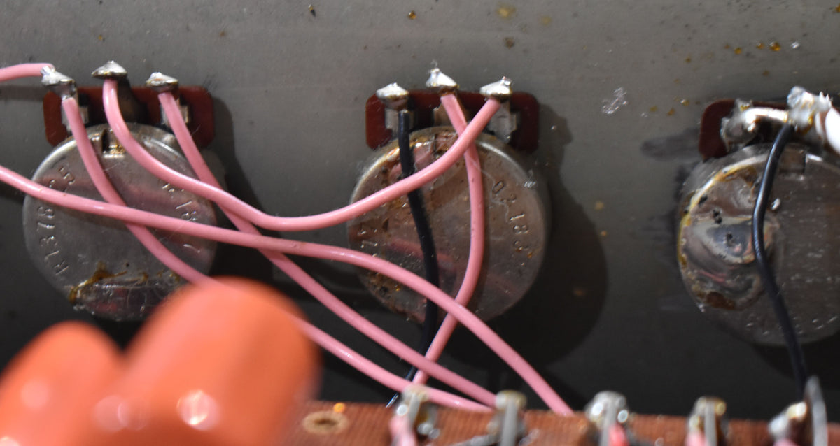 Close-up of three silver potentiometers with pink and black wiring, showing solder joints and some corrosion.