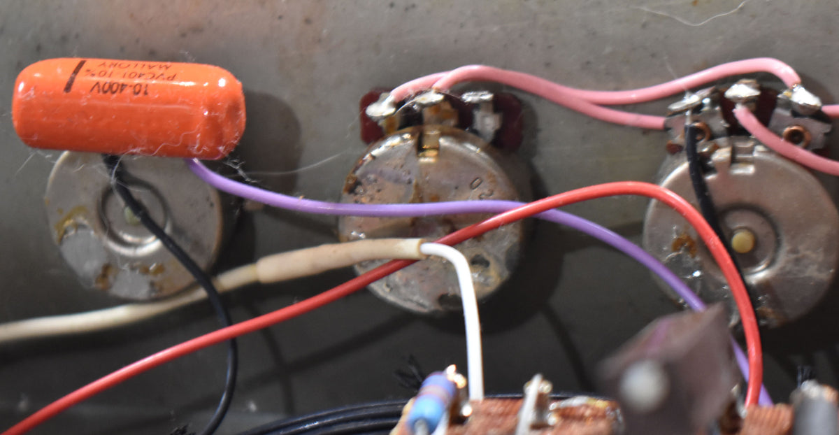 Close-up of the amp's internal wiring, showing three silver potentiometers with colorful wires, an orange capacitor, and visible dust.