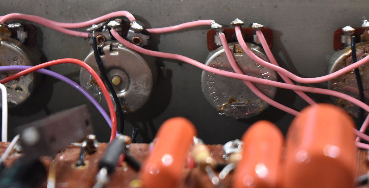 Close-up of the amplifier's internal wiring, showing several silver potentiometers connected by pink, red, purple, and black wires.