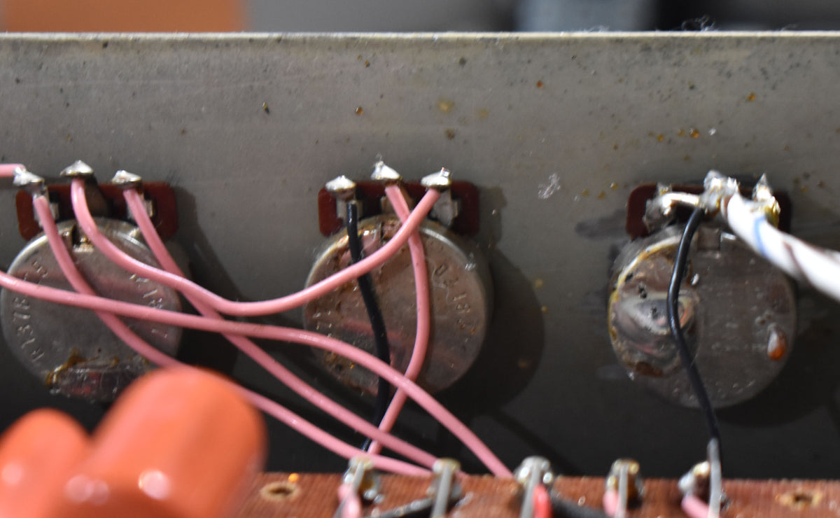 Close-up of three silver potentiometers with pink and black wiring, showing solder joints and a brown circuit board.