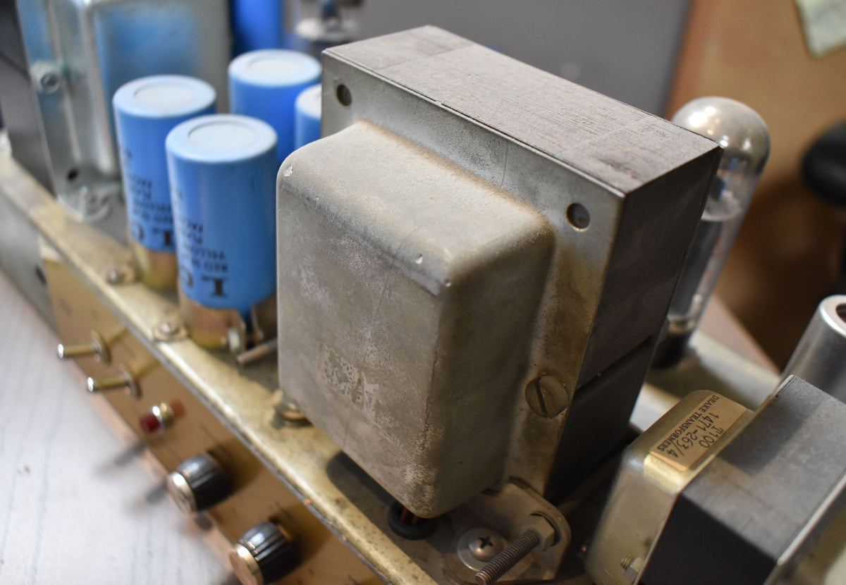 Close-up of the amp's dusty, worn metal chassis, showing large blue capacitors, a silver transformer, and two black control knobs.