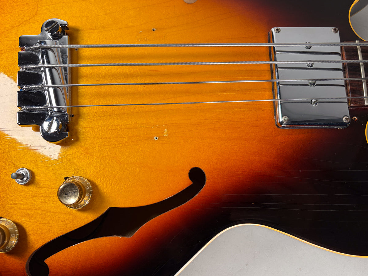 Close-up of the sunburst body, showing the chrome bridge, pickup, two gold control knobs, a switch, and an f-hole, with finish wear.