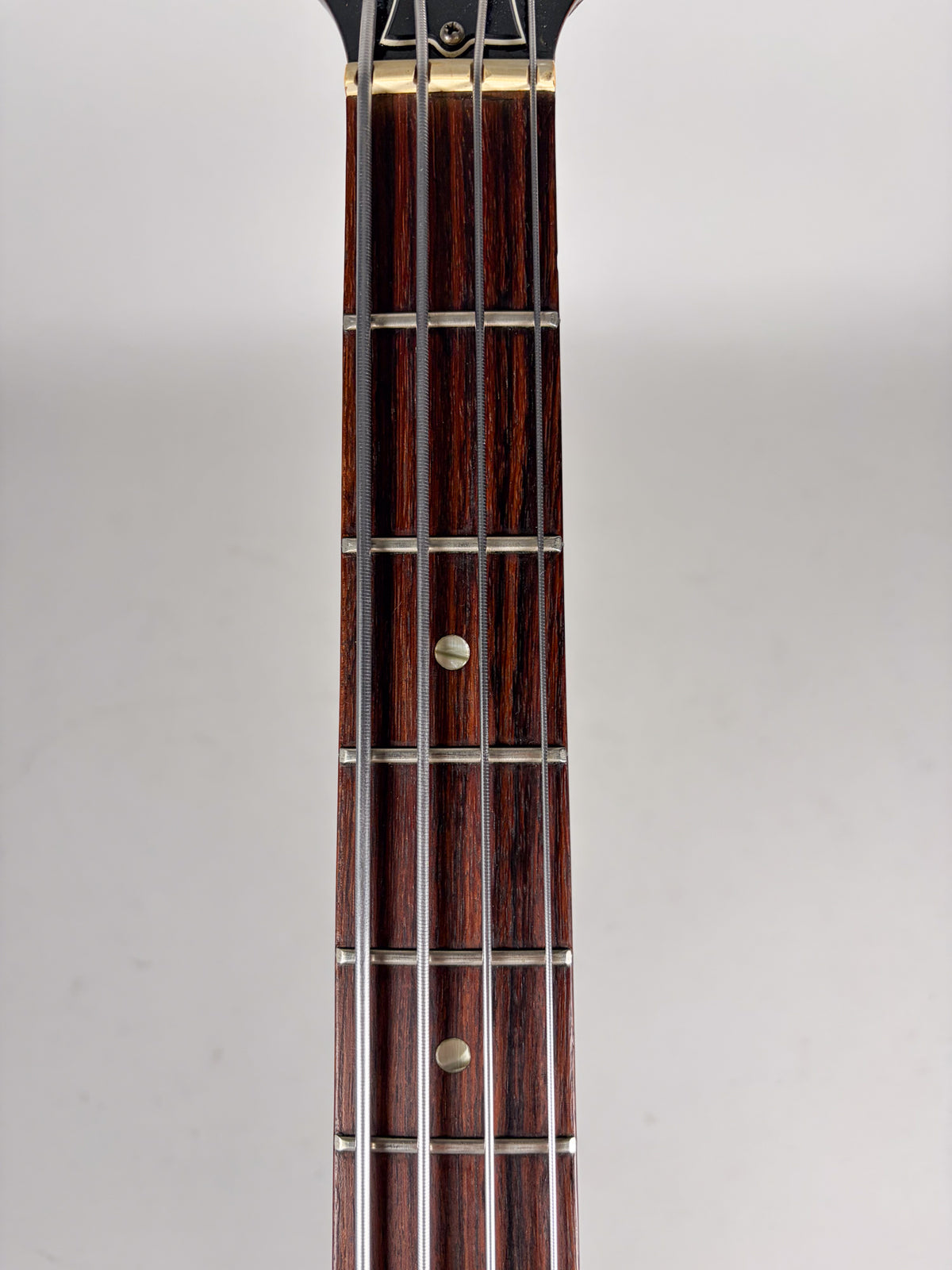 Close-up, top-down view of the dark rosewood fretboard with four strings, metal frets, and two round, pearloid fret markers.