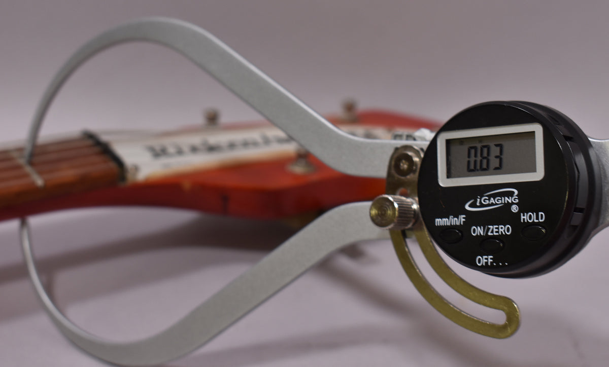 A digital caliper measures the string height at the first fret of the Fireglo guitar, showing 0.83mm.