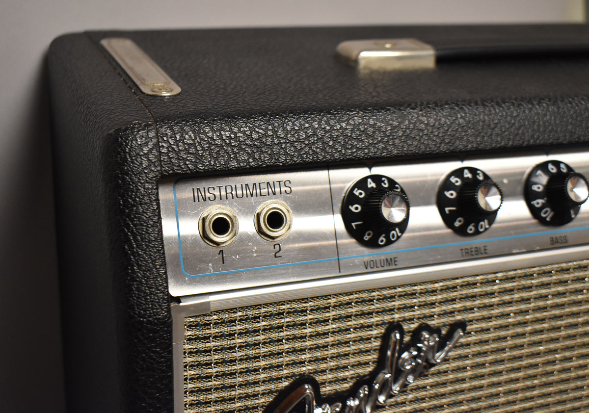 Close-up of the amp's black textured top and silver control panel with two input jacks, three black numbered knobs, and a silver handle.
