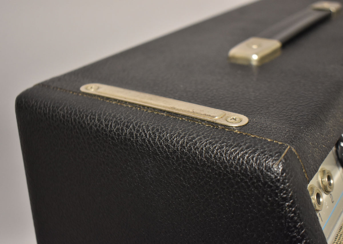 Close-up of the amp's black textured tolex, showing a worn metal vent strip, a leather handle, and light brown piping.