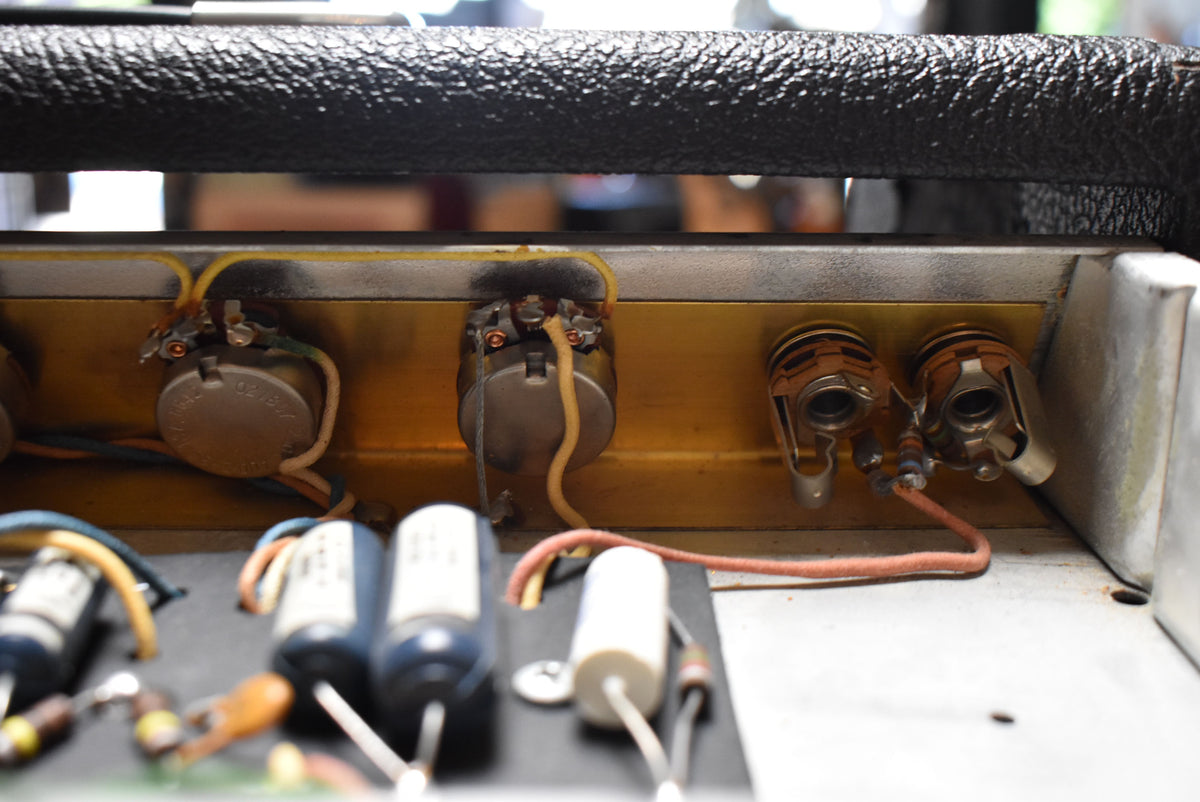 A close-up of the amp's internal wiring, showing several potentiometers, input jacks, and capacitors on a gold-colored chassis.