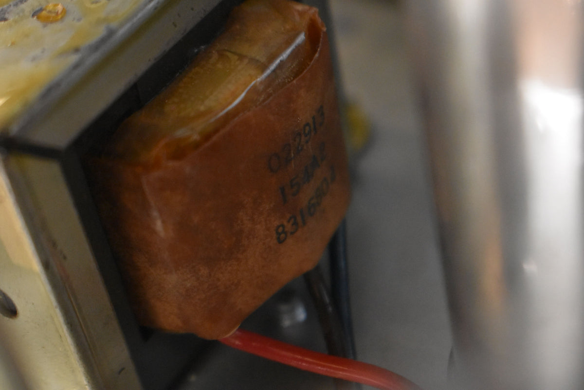 A close-up of an internal component, a brown paper-wrapped transformer with faded black numbers, and a red wire connected below.