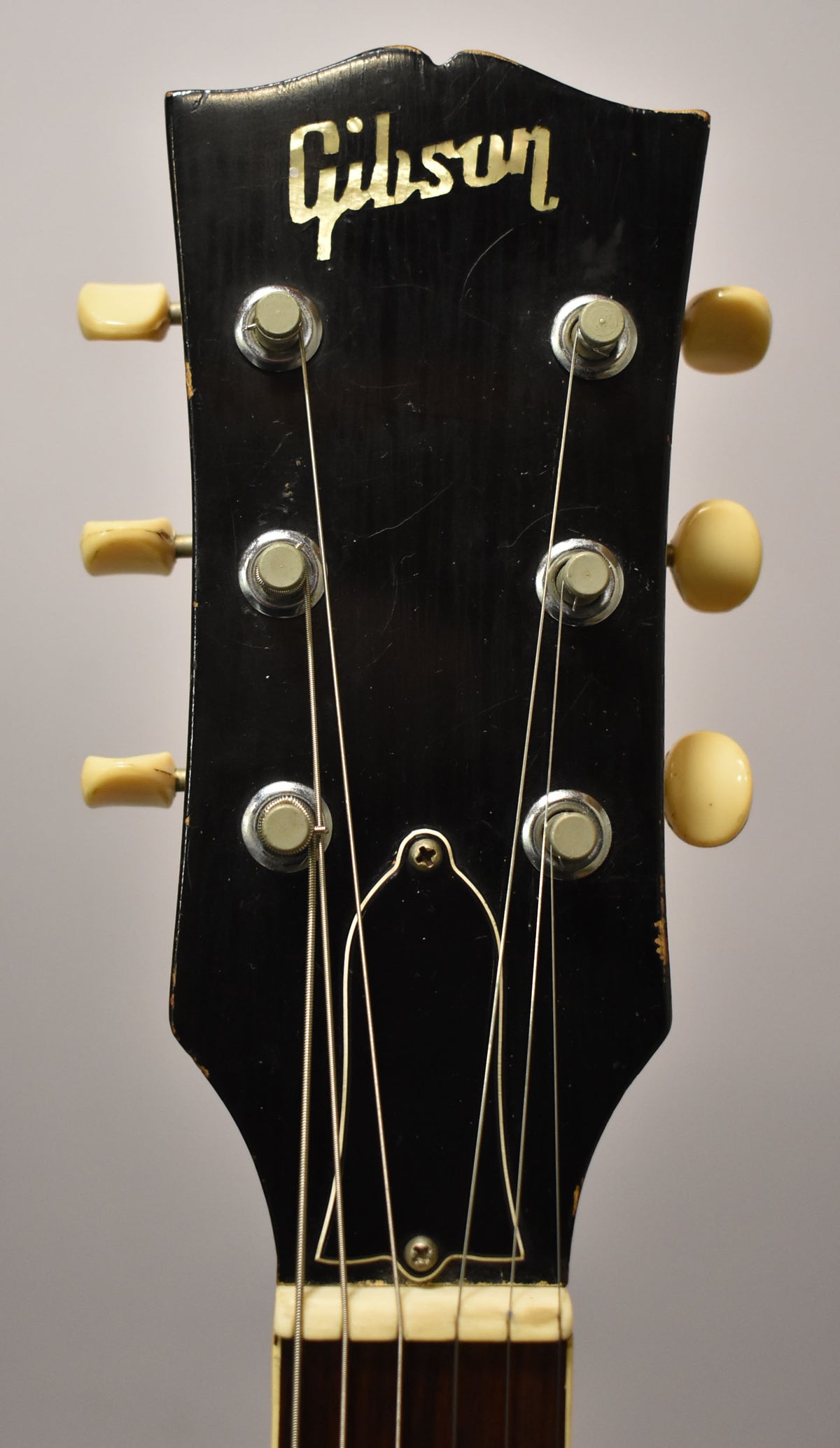 Close-up of the black headstock with six cream tuning pegs, showing wear on the edges and a gold logo.