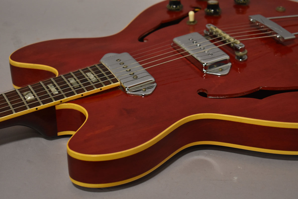 Close-up of the cherry red hollowbody guitar's lower bout and neck, showing two chrome P90 pickups, f-holes, and light finish wear.