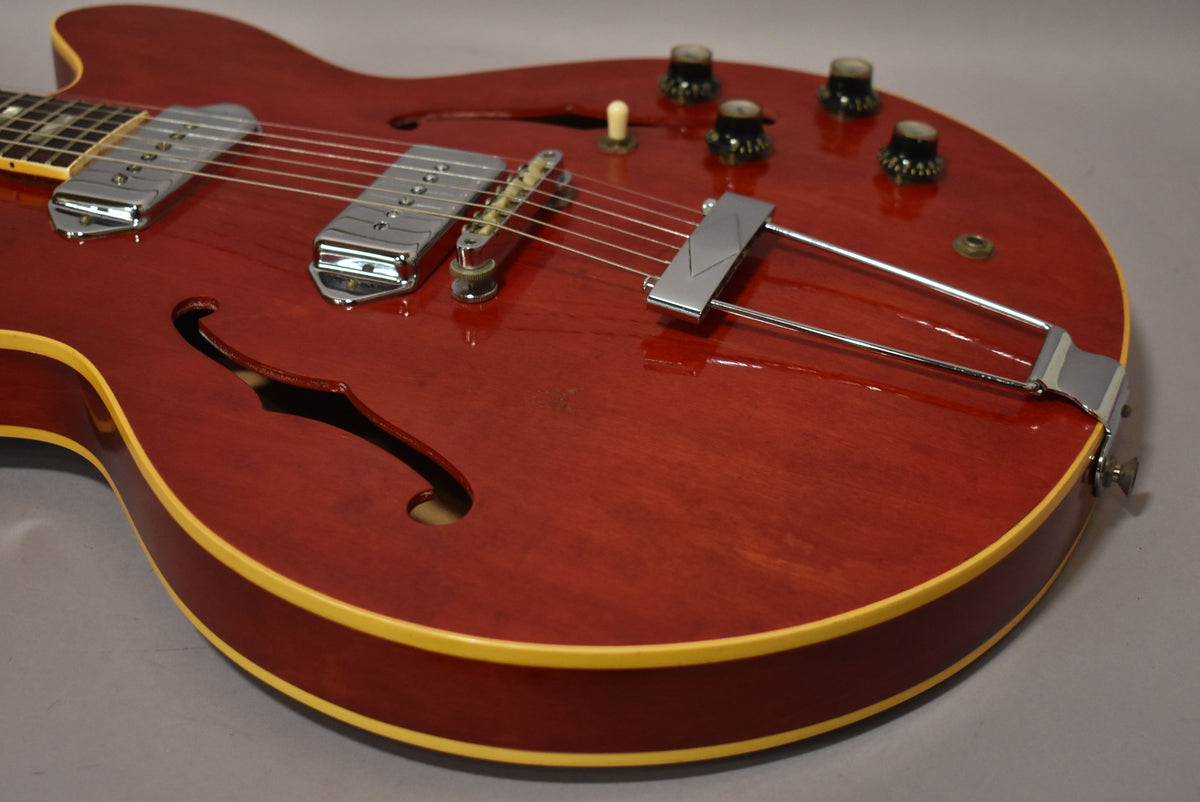 Close-up of the cherry red hollowbody's lower bout, showing two chrome P90 pickups, a trapeze tailpiece, and four black control knobs.