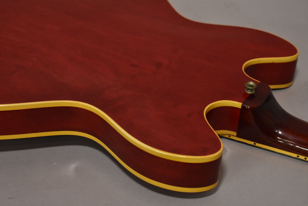 Close-up of the guitar's cherry red back and side, showing cream binding, a few small dings, and the neck heel.