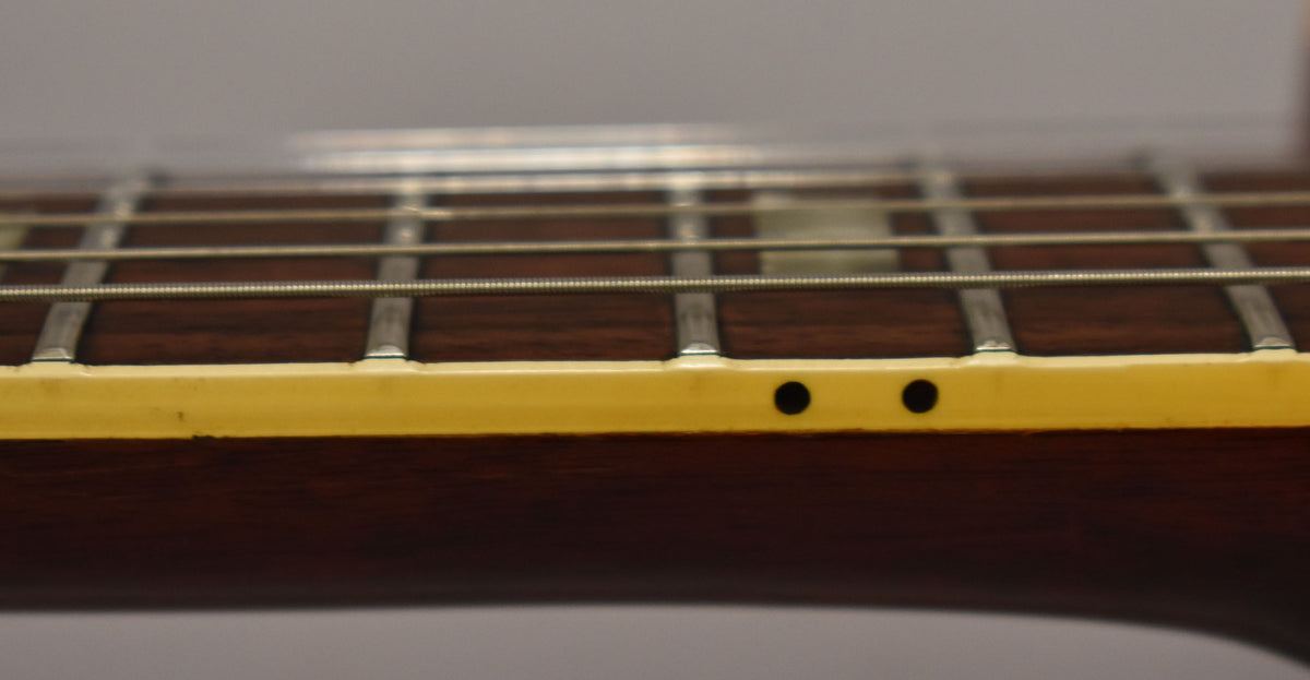 Close-up of the guitar's dark fretboard and frets, with two black side dot markers visible on the aged cream binding.