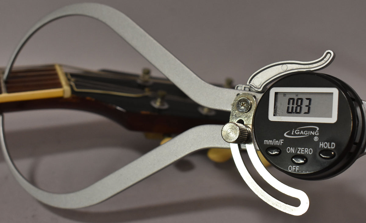 A close-up of the guitar's headstock and nut, with a digital caliper measuring the nut width at 0.83 inches.
