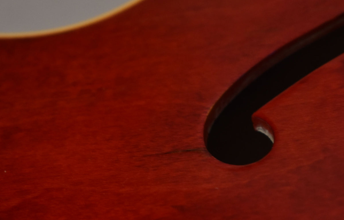 Close-up of the cherry red body with a black f-hole, showing a small dark scratch near the f-hole's curve.