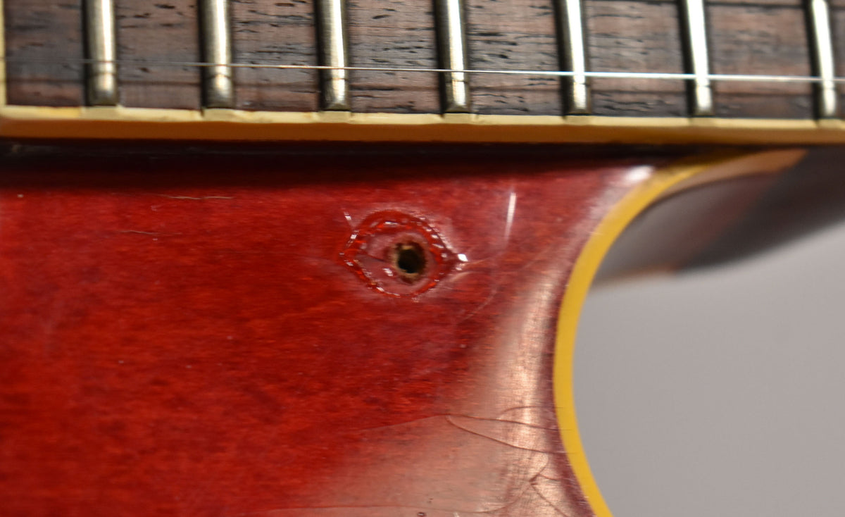 Close-up of the cherry red body near the neck joint, showing a strap button hole with chipped finish and extensive lacquer checking.