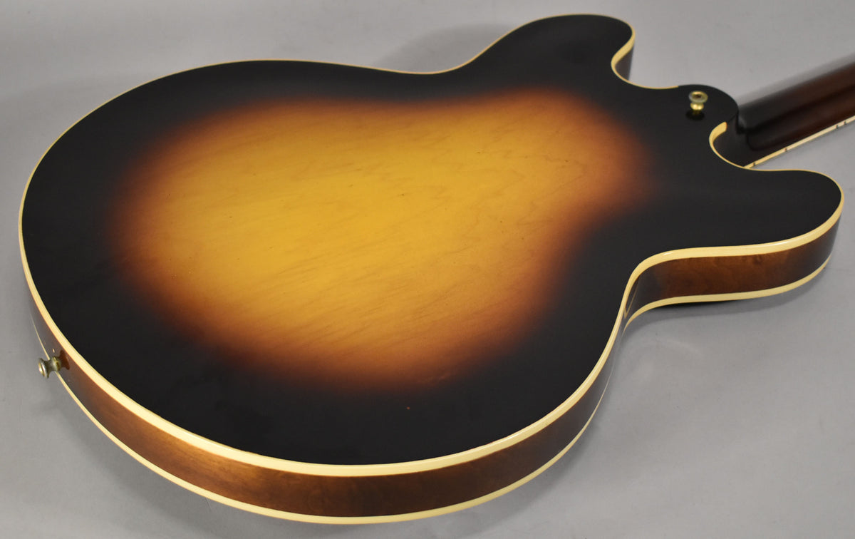 The guitar's sunburst back, with a bright center fading to dark edges, shows some light wear and a strap button near the neck joint.