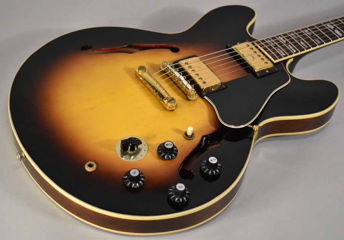 Close-up of the sunburst semi-hollowbody's lower bout, showing gold hardware, black pickguard, and four black control knobs.