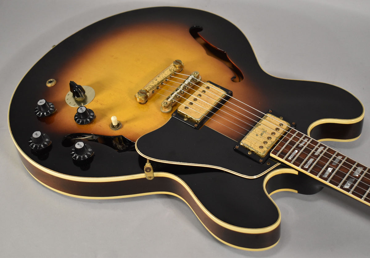 Sunburst semi-hollowbody guitar, angled from above, showing the body, pickguard, gold hardware, and lower fretboard.