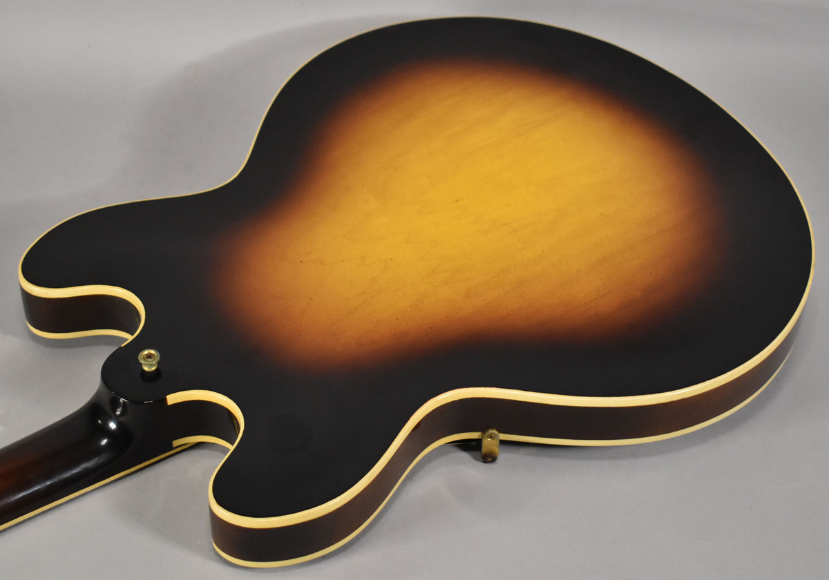 The guitar's sunburst back, with a dark brown edge fading to amber, shows light wear and a strap button near the lower bout.