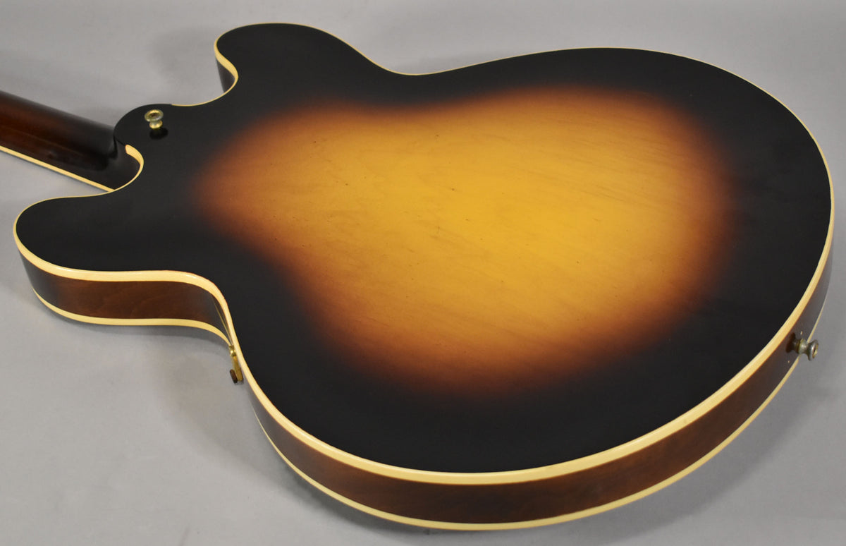 The guitar's sunburst back, with visible wear and checking, shows a strap button on the upper horn and another on the lower bout.