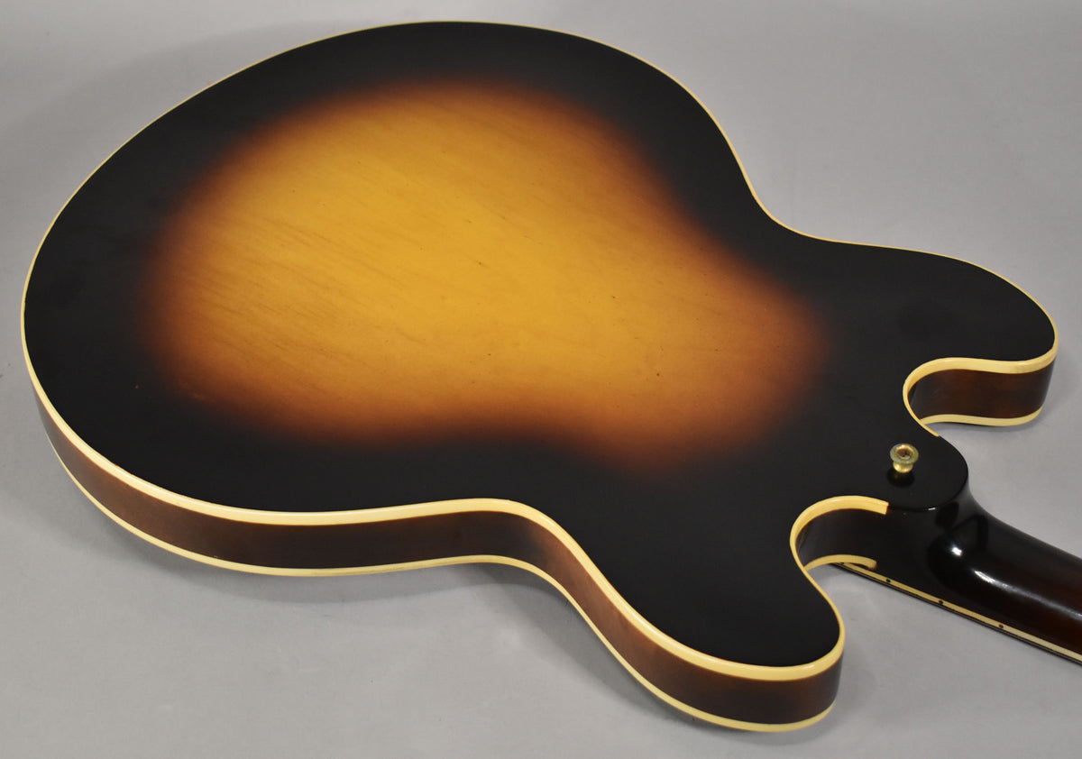 The guitar's sunburst back, with a dark brown edge fading to amber, shows light wear and a gold strap button near the neck heel.