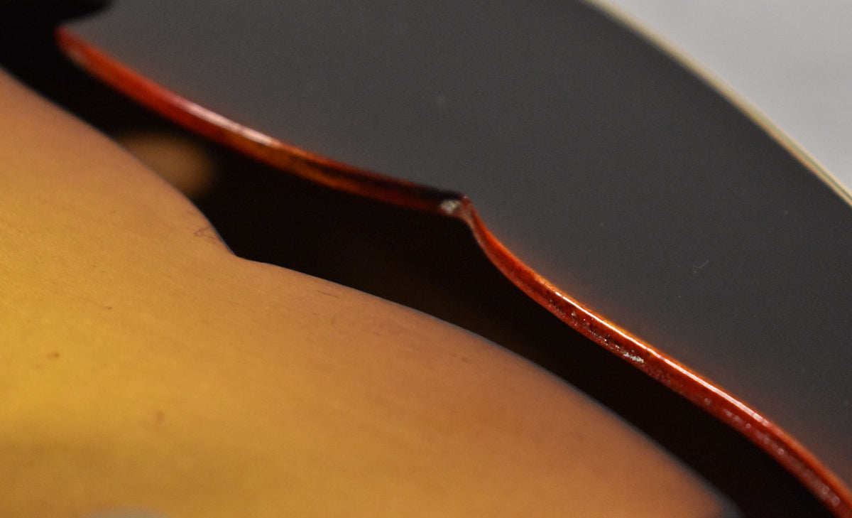 Close-up of the sunburst body's f-hole, showing the dark brown top, amber bottom, and a small chip on the f-hole's edge.