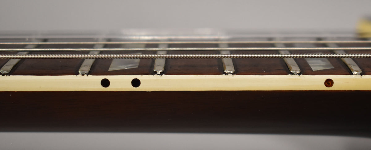 Close-up of the guitar's dark fretboard and light binding, showing three side dots and trapezoid inlays with visible fret wear.
