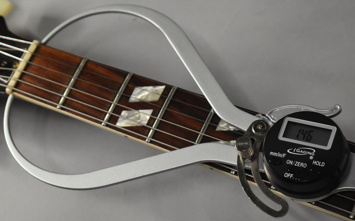 A digital fret rocker measures the dark rosewood fretboard with parallelogram inlays and light wear on the frets.