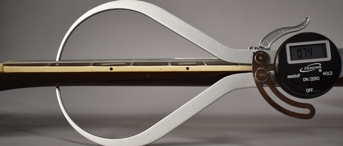 A digital caliper measures the guitar's dark brown neck and cream binding, showing "0.74" on its black display.