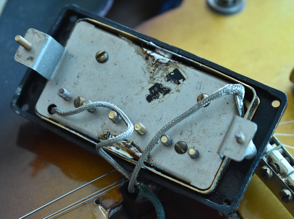 Close-up of the underside of a pickup, showing its metal baseplate, braided wire, mounting bracket, and worn label.