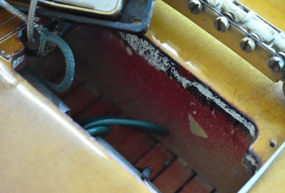 Close-up of the guitar's interior, revealing red paint, exposed wood, and wiring, with a pickup and bridge visible.