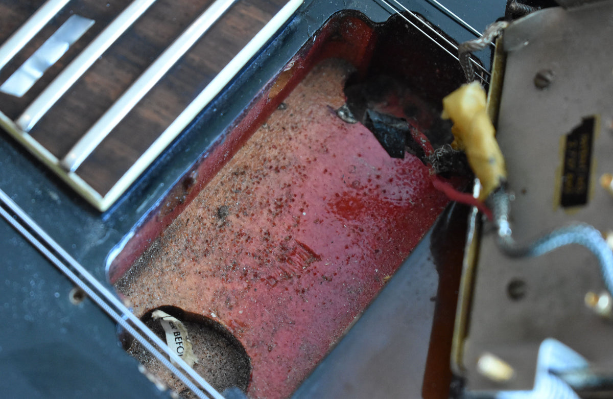 Close-up of the guitar's control cavity, revealing a worn, reddish-brown interior with exposed wiring and a partial label.