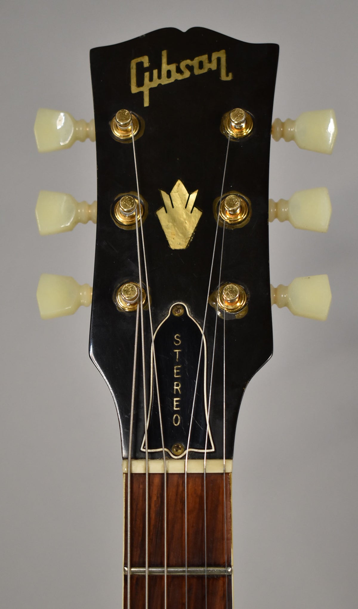 Close-up of the black headstock with gold tuning pegs and cream buttons, showing a gold crown inlay and "STEREO" on the truss rod cover.