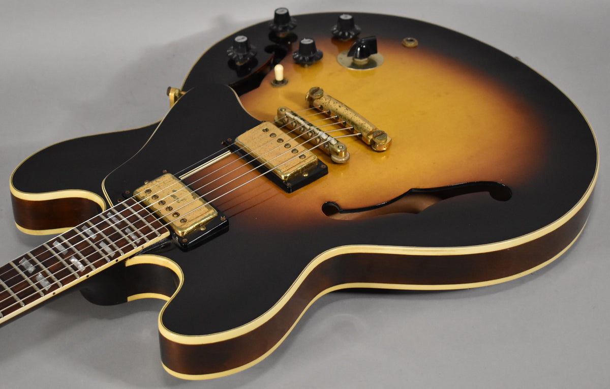 Upper body of a sunburst semi-hollow guitar, showing gold hardware, f-hole, and cream binding with some wear.