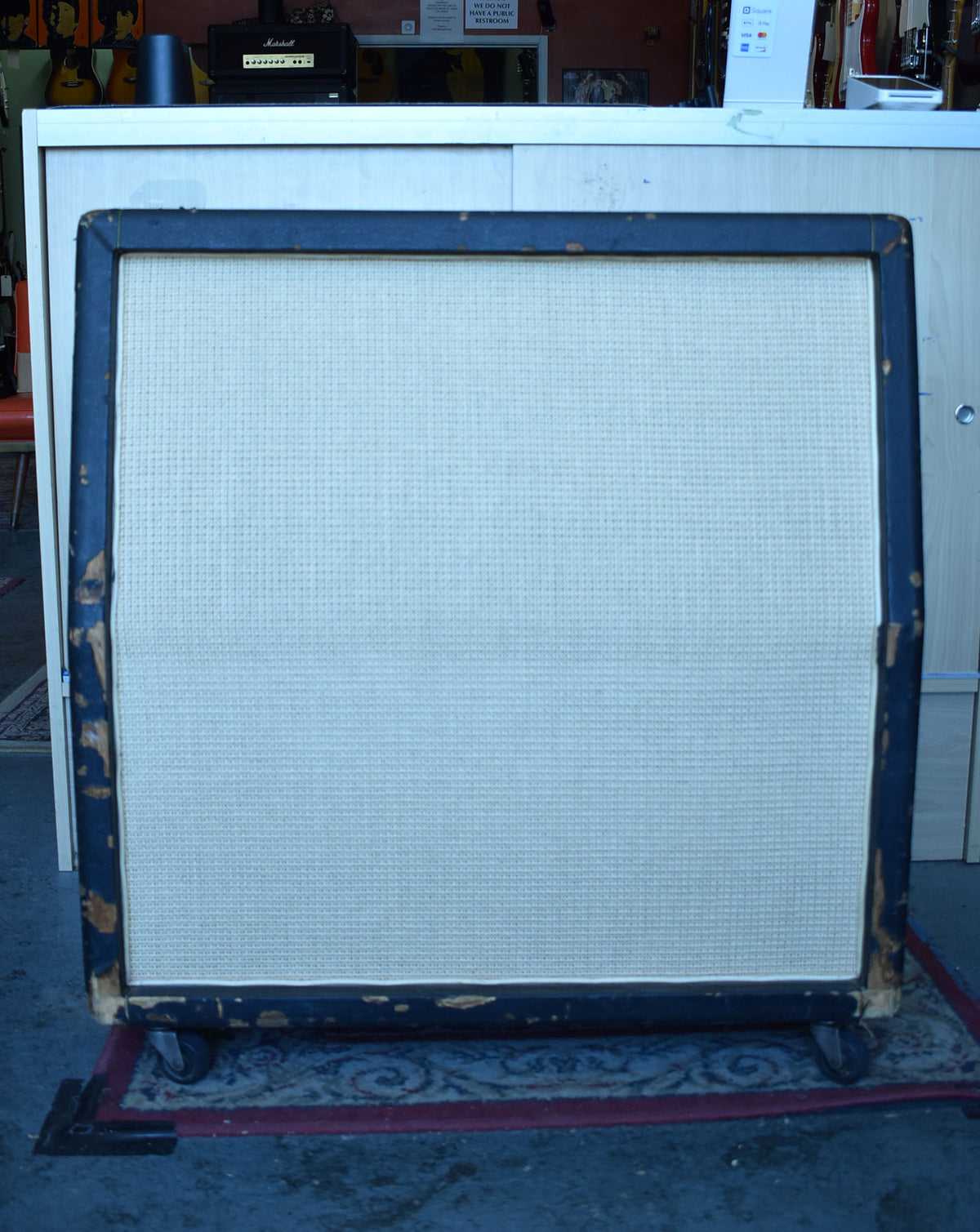 Front view of a vintage Marshall 4x12 cabinet with a light-colored basketweave grille cloth and heavily worn black tolex, showing exposed wood.