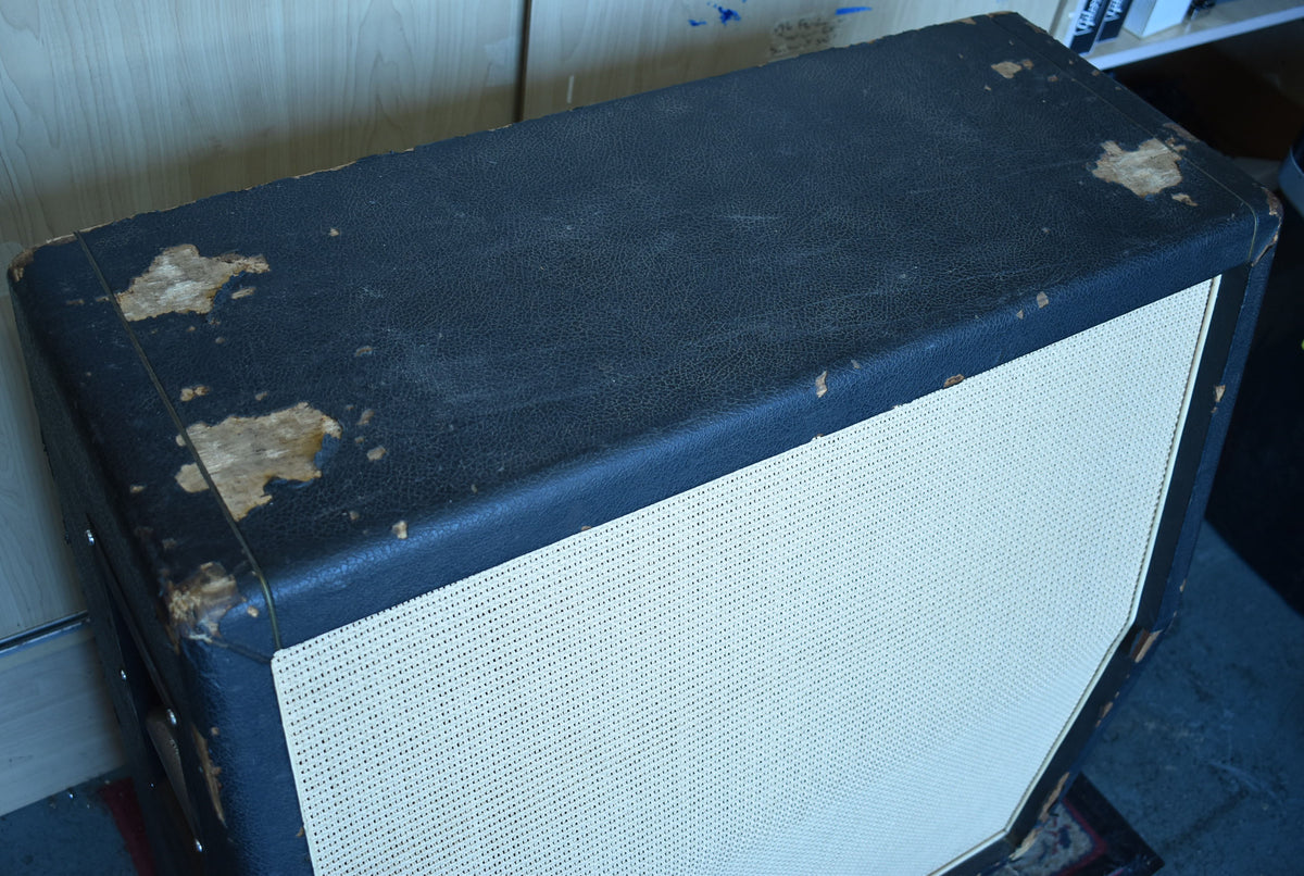 The top and front of a black basketweave cabinet with a light-colored grille, showing significant tolex wear on the top edges.