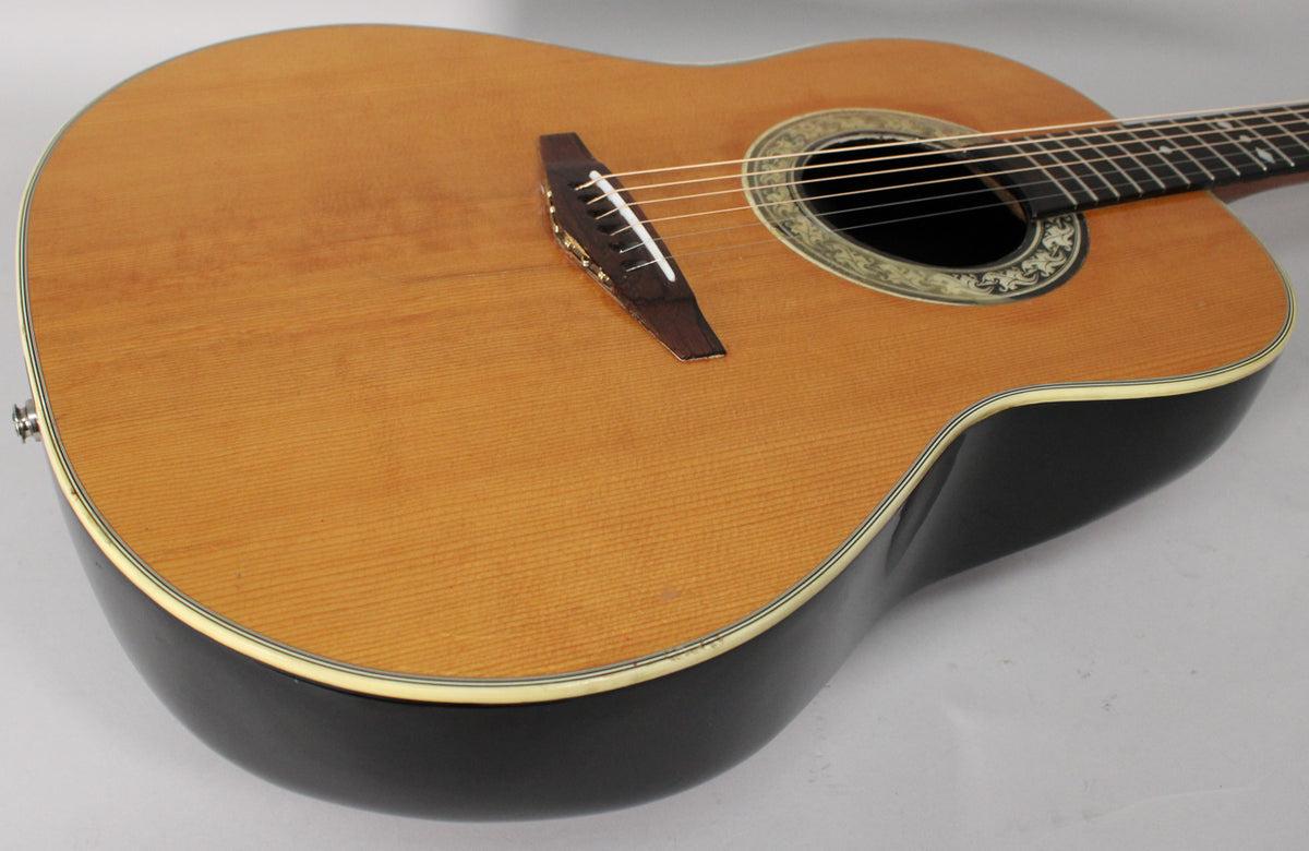 The guitar's light wood top and dark, shiny bowl back are visible, with a decorative rosette around the soundhole and a strap button.