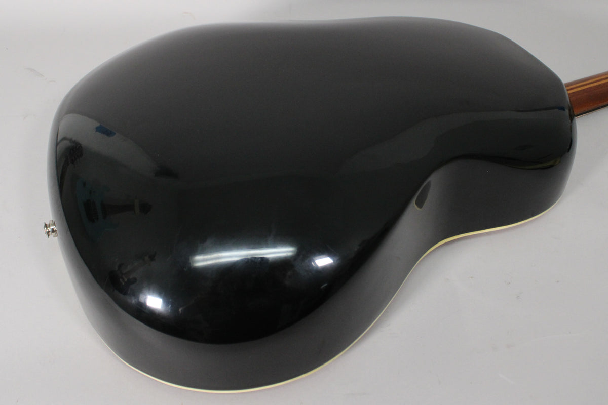 The guitar's shiny black bowl back is angled from the lower right, showing a chrome endpin jack and some minor surface wear.