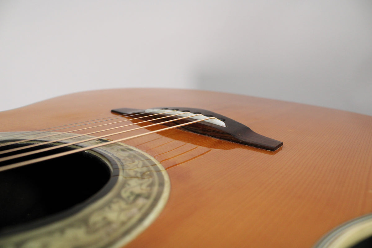 Close-up of the shiny, light brown acoustic guitar's body, showing the soundhole with ornate rosette and the dark wood bridge.