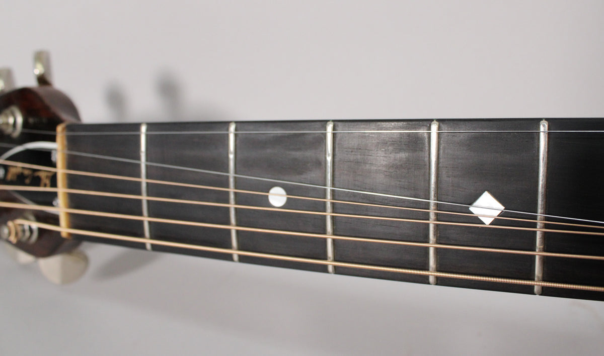 Close-up of the dark fretboard with a white dot inlay at the 7th fret and a diamond inlay at the 9th fret, showing light string wear.