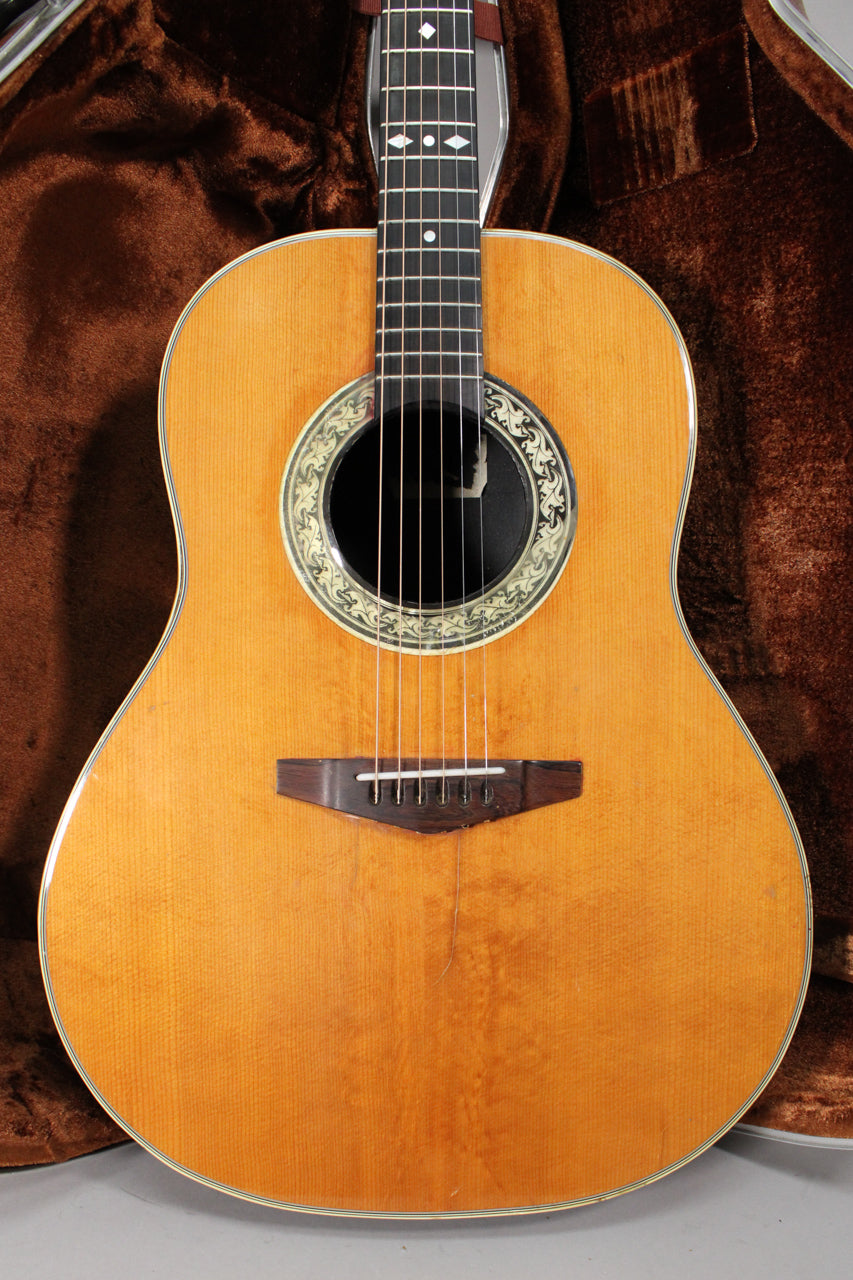 The light-colored acoustic guitar is centered, showing its body and neck, with a decorative soundhole rosette and dark bridge.