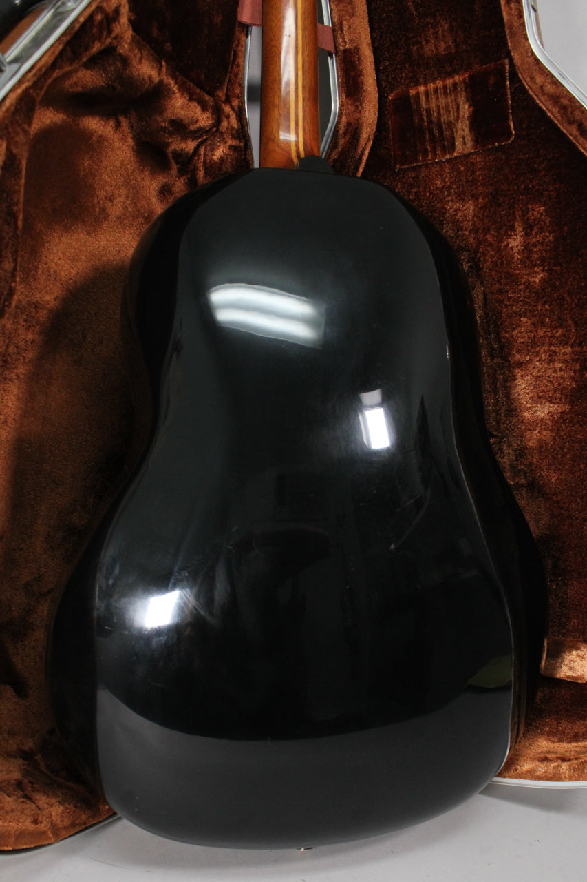 The guitar's shiny black bowl back and lower neck are visible, resting in a brown plush-lined hard case.
