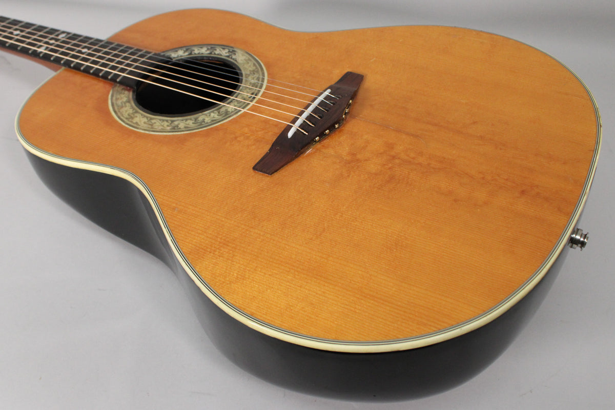 The acoustic-electric guitar's light wood top and dark bowl back are visible from the upper bout, with a decorative rosette.