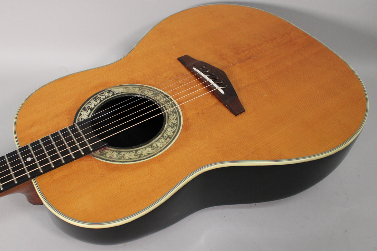 The guitar's light brown top and black bowl back are shown from above, with a decorative soundhole rosette and dark bridge.