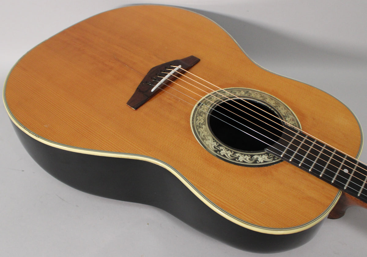 The guitar's light brown top and dark bowl back are visible from above, with a decorative soundhole rosette.